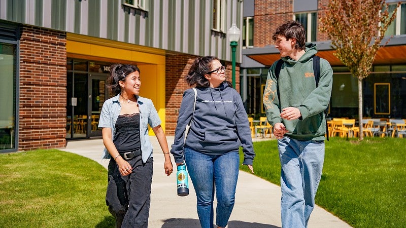 three members of the media and social action academic residential community walk through a UO residence hall courtyard