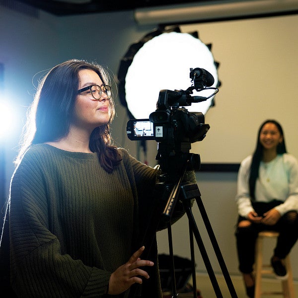 a student adjusts a video camera in the Allen Hall studio