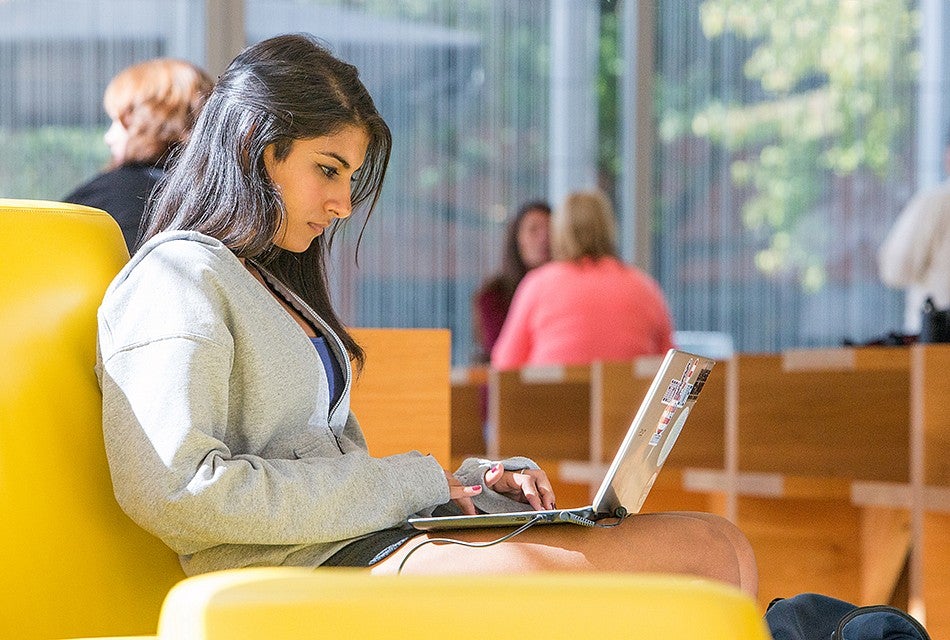 A female student working on a laptop while sitting on a couch