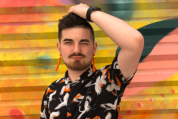student wearing colorful shirt and earrings, posing in front of colorful mural