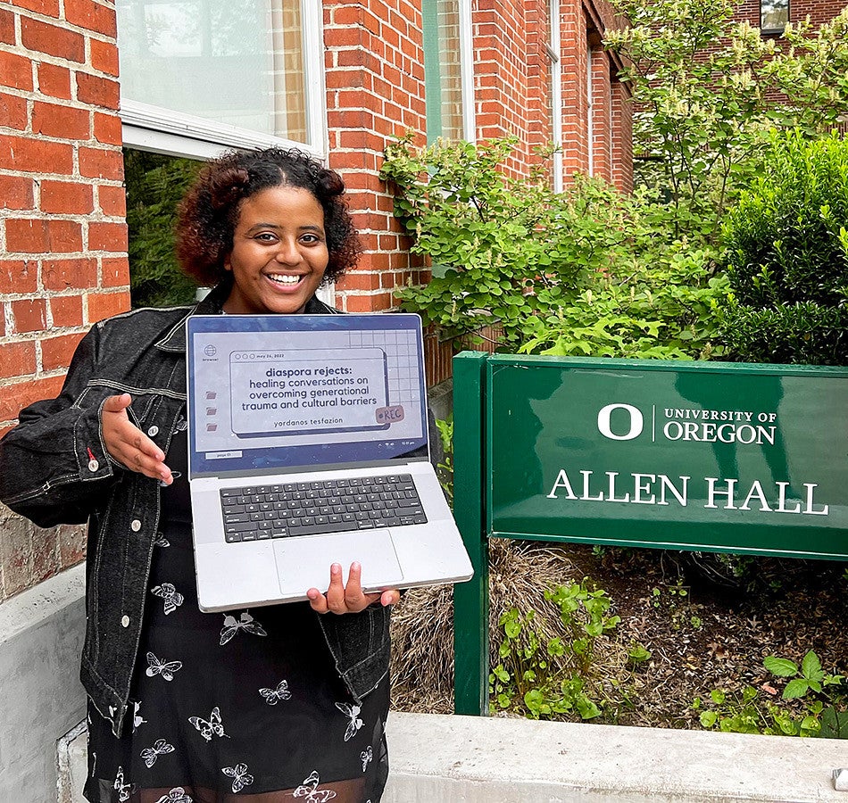 Yordanos Tesfazion poses with a laptop in front of the Allen Hall sign on the University of Oregon campus