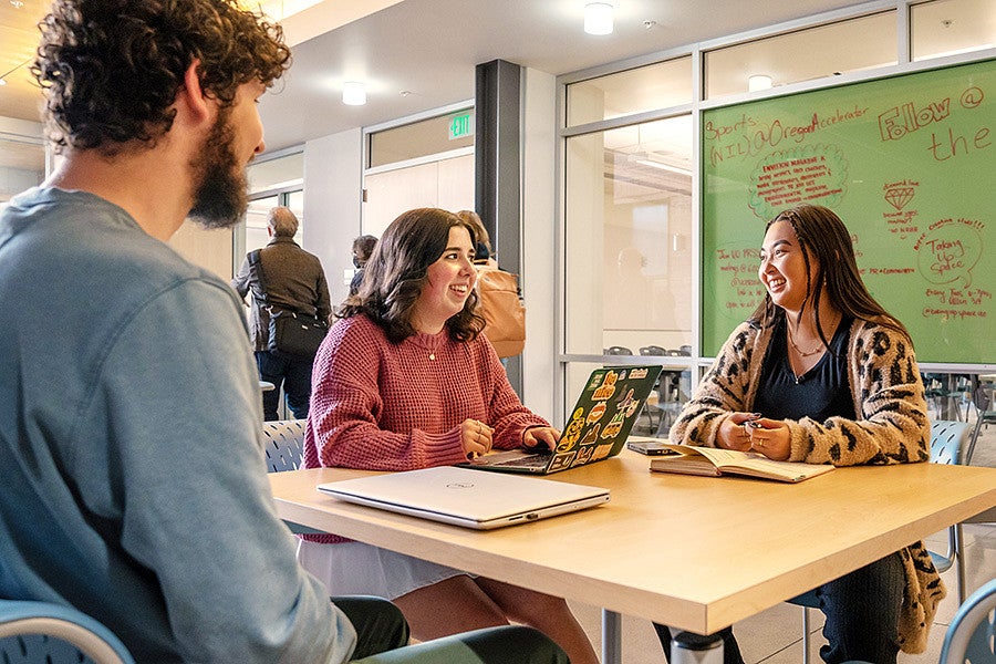 three students sit at a table in the Allen Hall atrium