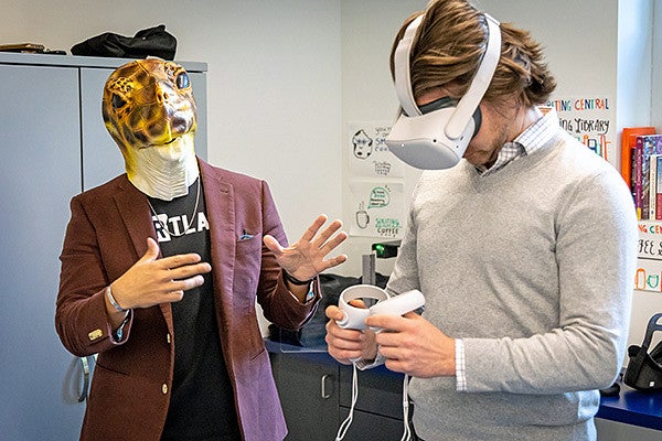 Danny Pimentel, wearing a turtle mask, instructs a student wearing a VR headset