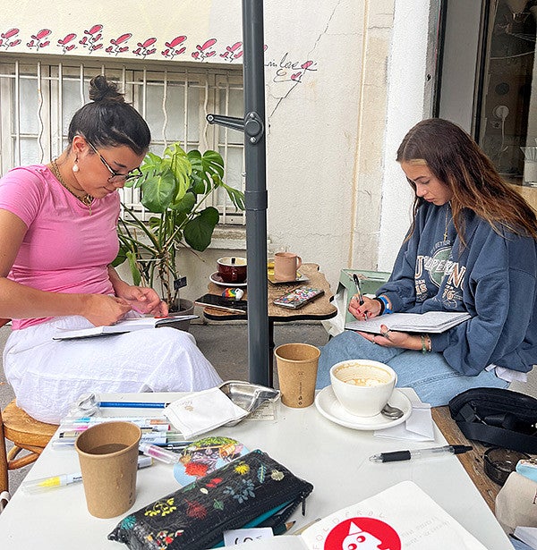 two SOJC students journal at a cafe in Paris