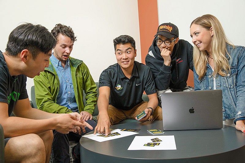 Five master's students sit around a table looking at printed cards