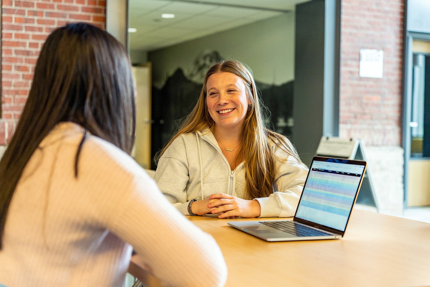 Erin Tooley chats with another student while they sit at a table with an open laptop in front of them