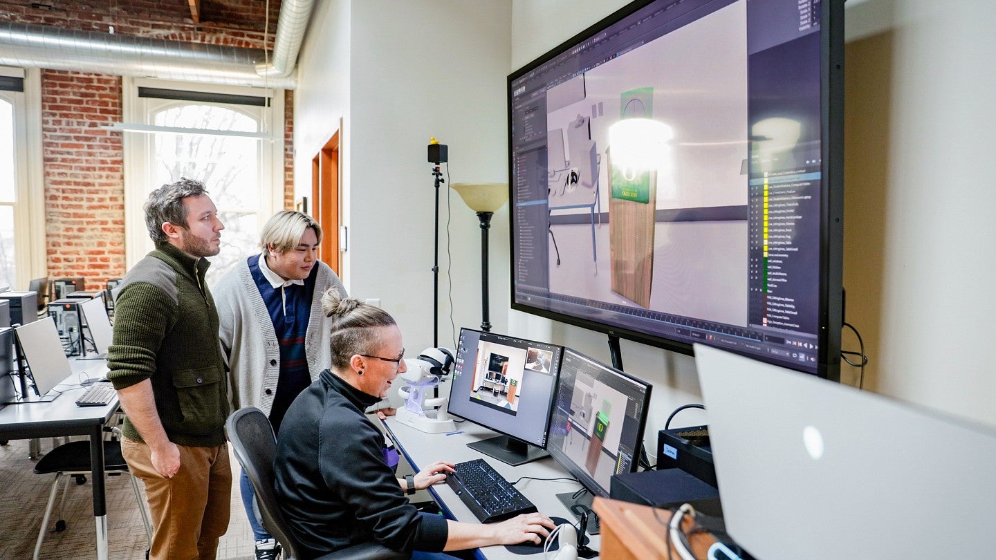 Nikki Dunsire and two students review a virtual environment on computer monitors