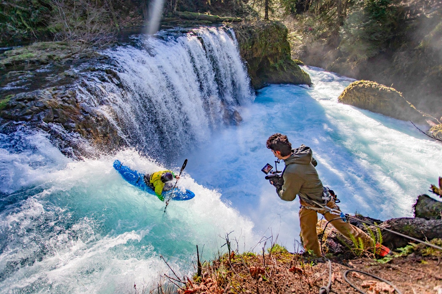 Dan Teitelbaum leans out above a waterfall to film a kayaker 