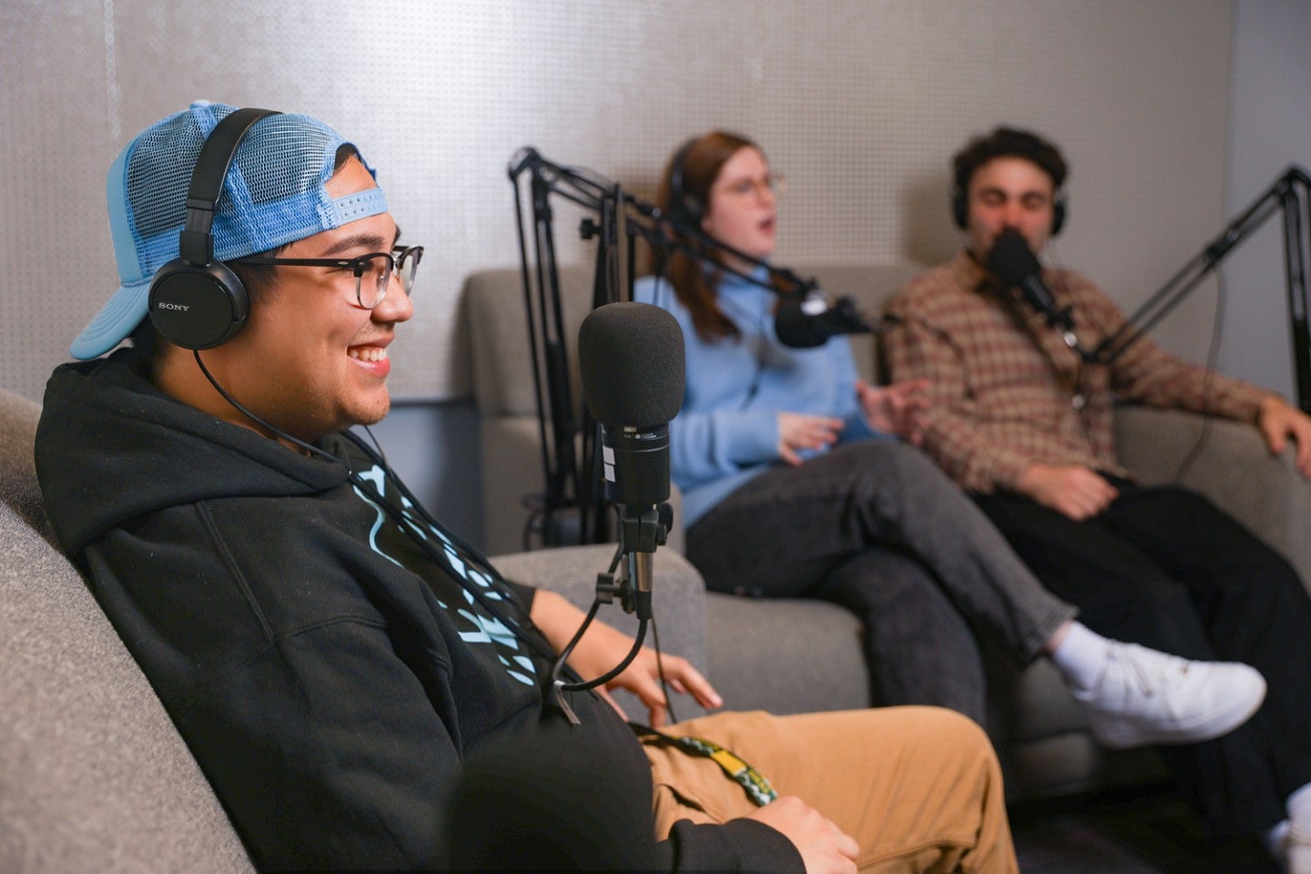 three students sit on couches in the University of Oregon School of Journalism and Communication's podcasting studio with microphones in front of them