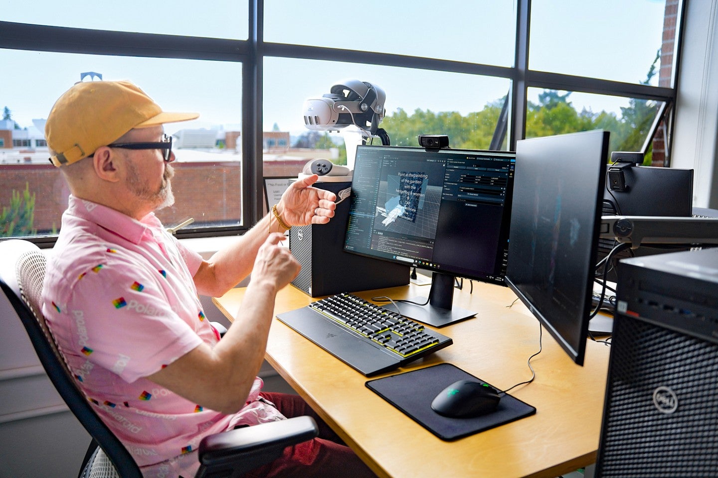 Jason de Parrie-Turner mimes scrolling through a cell phone while planning an augmented reality project and sitting in front of a computer with dual monitors in the Oregon Reality Lab
