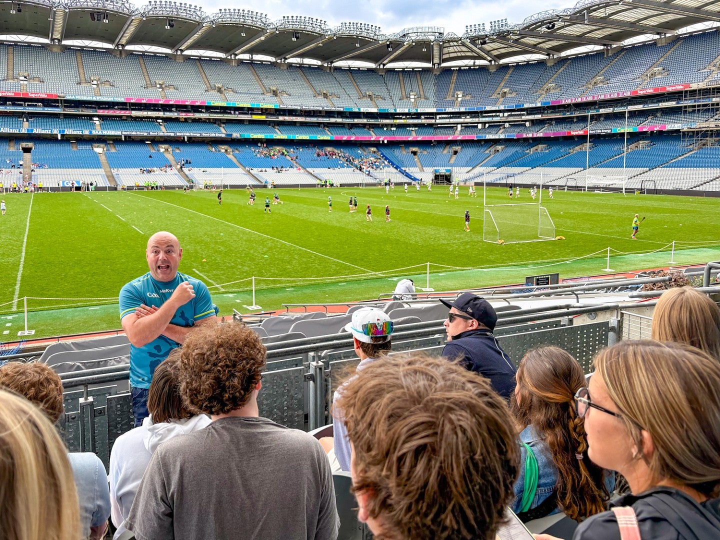 Students look out over the field of Croke Park stadium while a tour guide stands in front of them, facing the camera