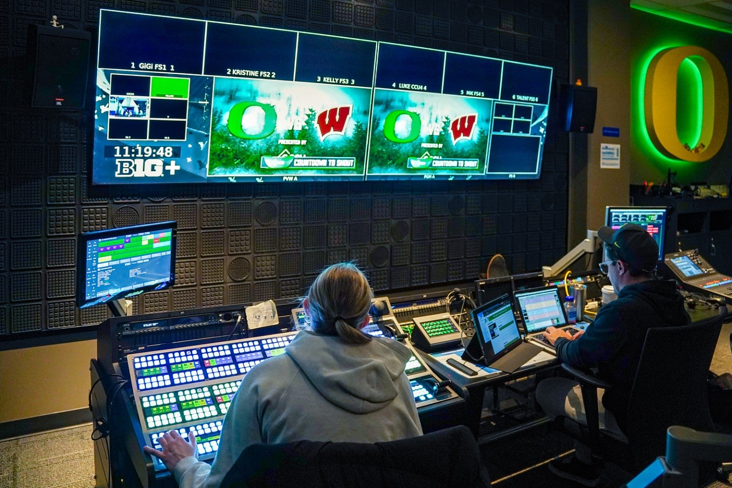 Student producers work at control boards in front of large monitors mounted on the wall