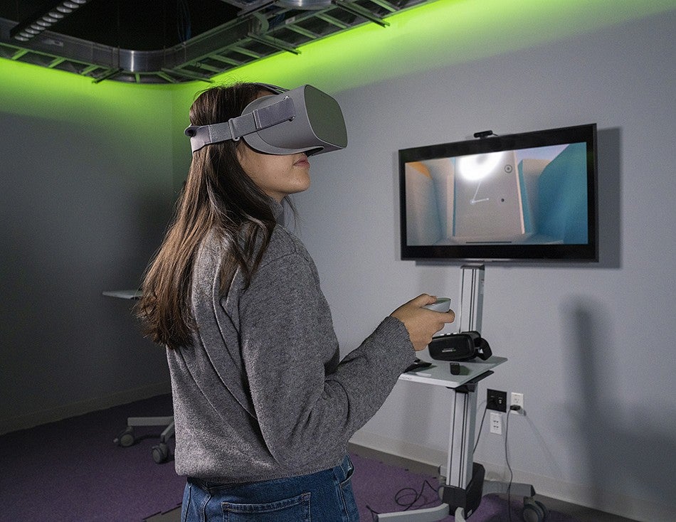 Student wears VR goggles while inside of the immersive media lab. 