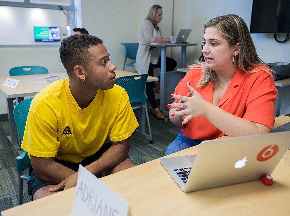 An SOJC writing coach works with a student in the Writing Lab. Both people are seated at a table, and a laptop is open in front of them. 