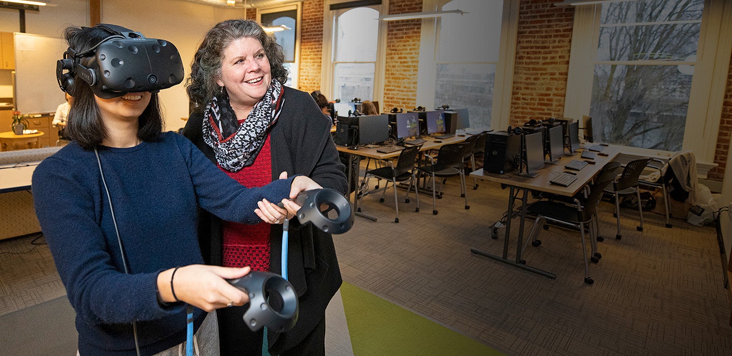 female student using wearable VR technology, assisted by female professor