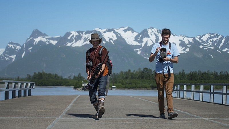 two male students with camera equipment with mountains in the background