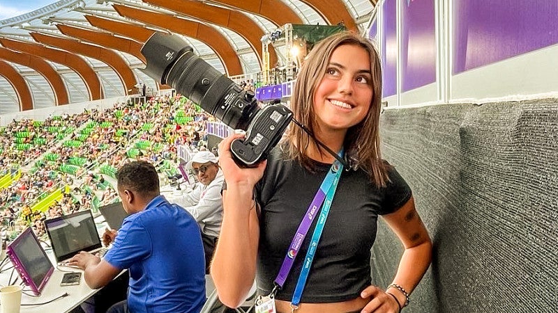 Chloe Montague holds up a camera while standing in the press area of Hayward Field