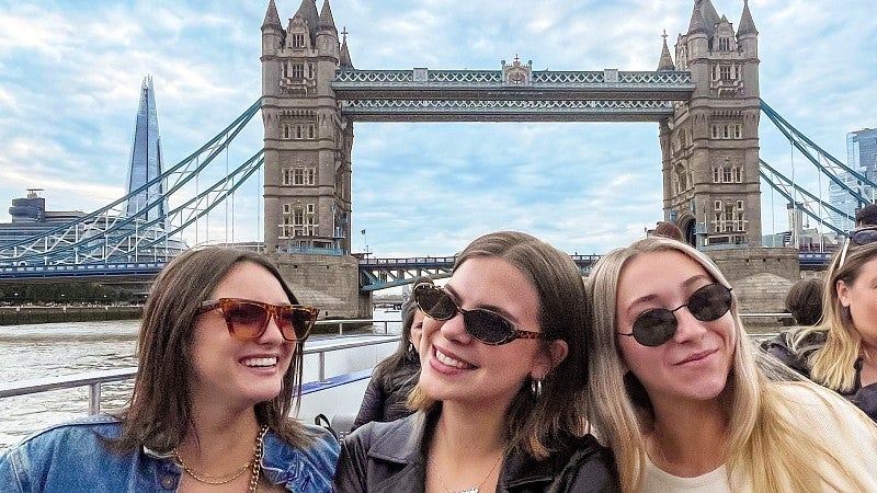 three students pose in front of a bridge in London