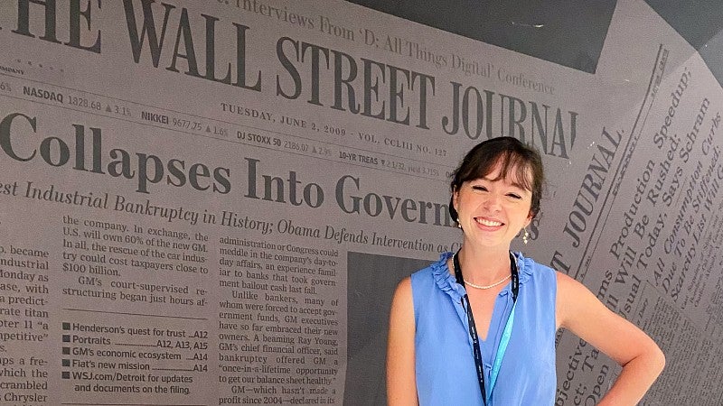 Sierra McClain poses in front of a wall with images of the Wall Street Journal