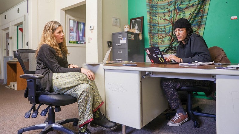 Camilla Mortensen and Faheem Kahn sit in office chairs and work on laptops across a desk from each other