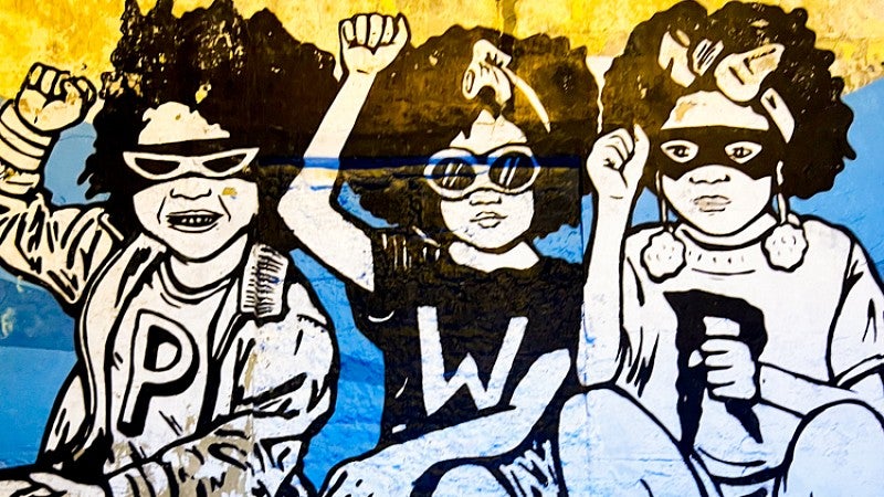 a mural showing three young Colombian girls holding up their fists in front of background of the Colombian flag 