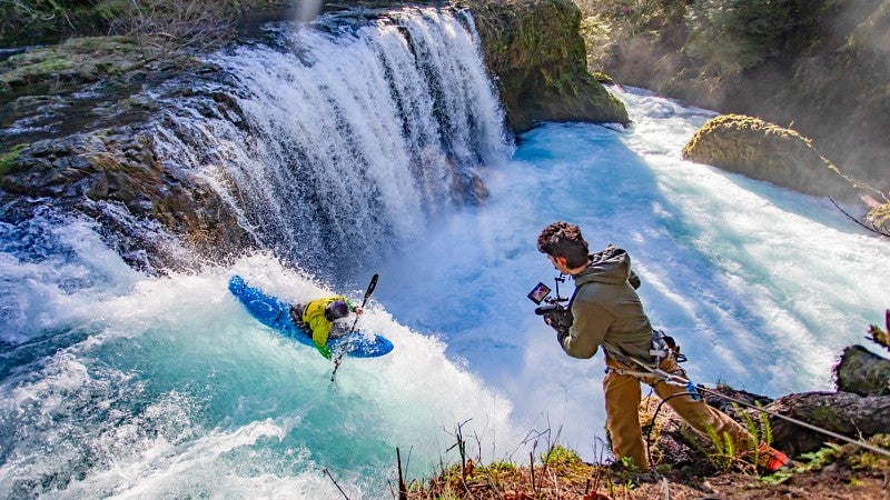 Dan Teitelbaum leans out above a waterfall to film a kayaker 