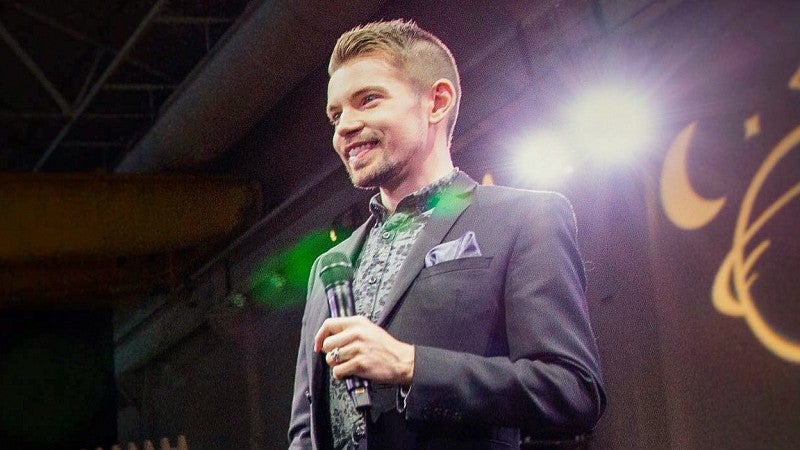 Galen Ettlin holds a microphone with a stage light shining over his shoulder