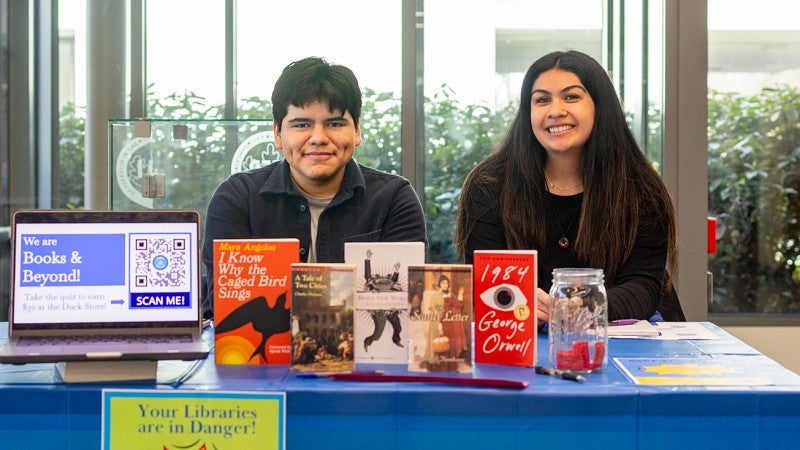 two members of the SOJC PR student competition team sit at a table displaying banned books