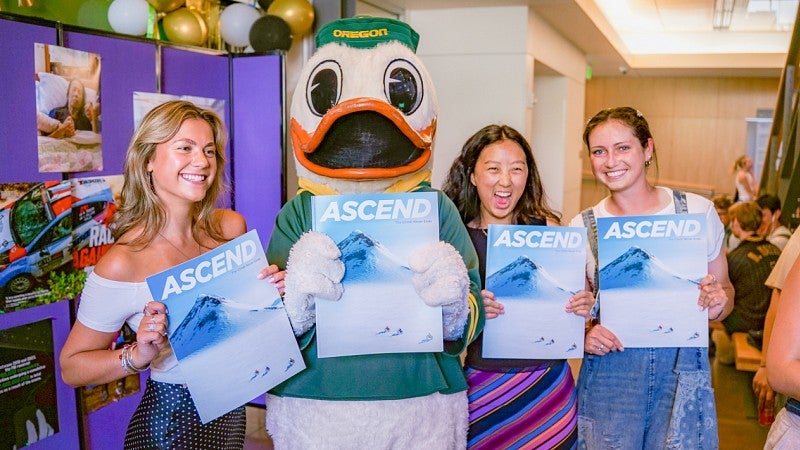 three students and the Oregon Duck pose while holding copies of Ascend Magazine