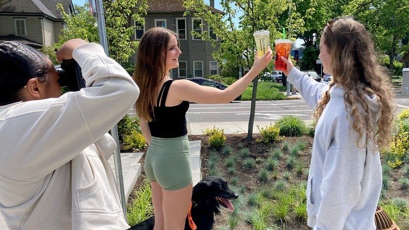 an SOJC student photographs two UO student athletes clinking cups as part of an NIL campaign for Dutch Bros.