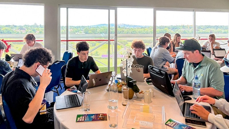 groups of University of Oregon School of Journalism and Communication students sit around tables writing stories on laptops in front of large windows framing a countryside view of Ireland