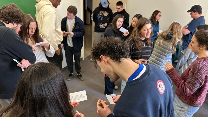 a large group of students stand discussing notes in pairs