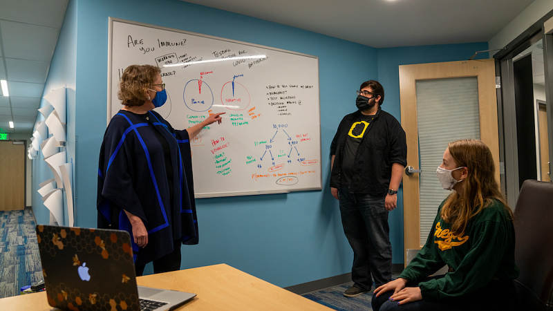 Three people conversing in front of white board with plans for coronavirus information story. 