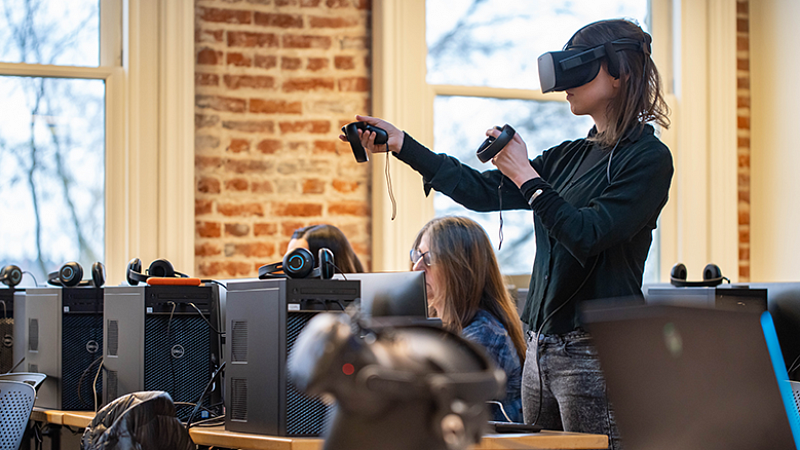 a student wearing VR gear stands among a row of computers