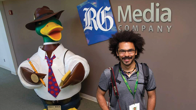 2021 Snowden intern Jeremy Williams poses with a large reporter duck sculpture and the RG media sign