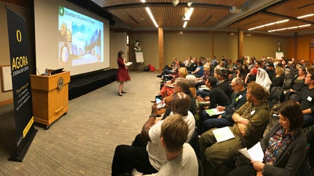 Woman presents in front of crowd in auditorium at the Agora Journalism Center