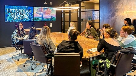 a group of students sit around a conference table in front of a screen that says "let's break into q&a groups"