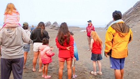 Sof Fox, a UO science communication minor, talks to a group of people standing on an Oregon beach