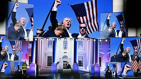 Donald Trump surrounded by screens showing him raising his fist