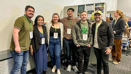 a group of graduate students including Luke Walker, and Assistant Professor Danny Pimentel, pose in front of a research poster