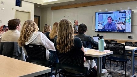 students looking at a large screen showing a person on Zoom