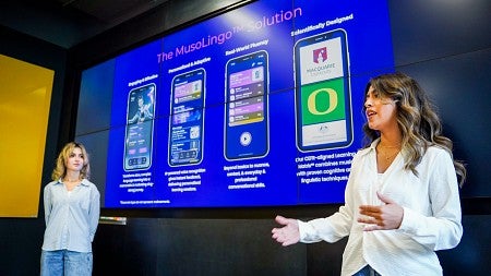 two students present a project proposal in front of a large digital screen