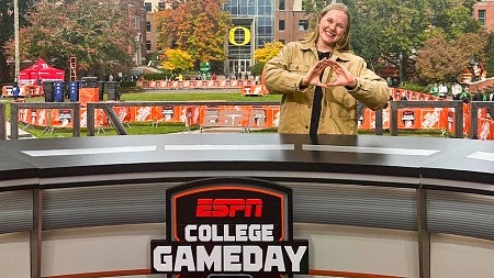 Sophie Fowler poses and throws her O from behind the ESPN College Gameday desk on the University of Oregon campus