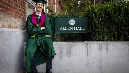 SOJC student sitting next to Allen Hall sign.