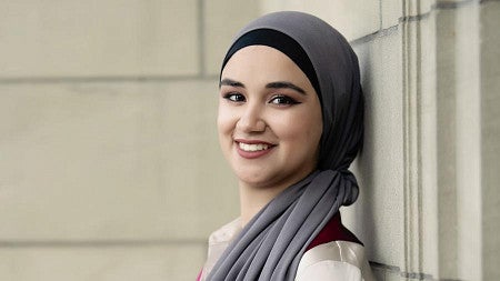 Hanin Najjar, wearing hijab and leaning against a wall, smiles for the camera.