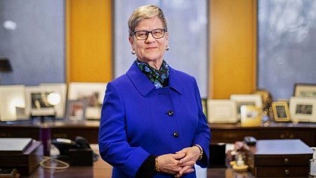 Kathleen Hall Jamieson is wearing a blue suit and standing in front of desks.