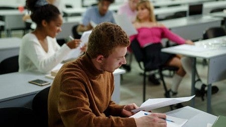 A student looks at an assignment while their classmates converse behind them. 