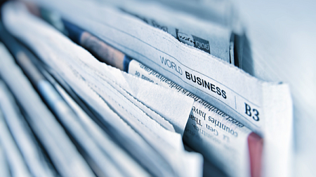 A stack of newspapers on a table in front of a window.