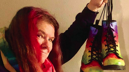 Bethany Grace Howe stands with pink hair holding colorful boots.
