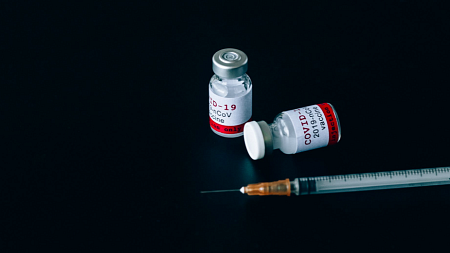  Two vials of the COVID-19 vaccine sit on a black table next to a syringe (Photo credit - Nataliya Vaitkevich)